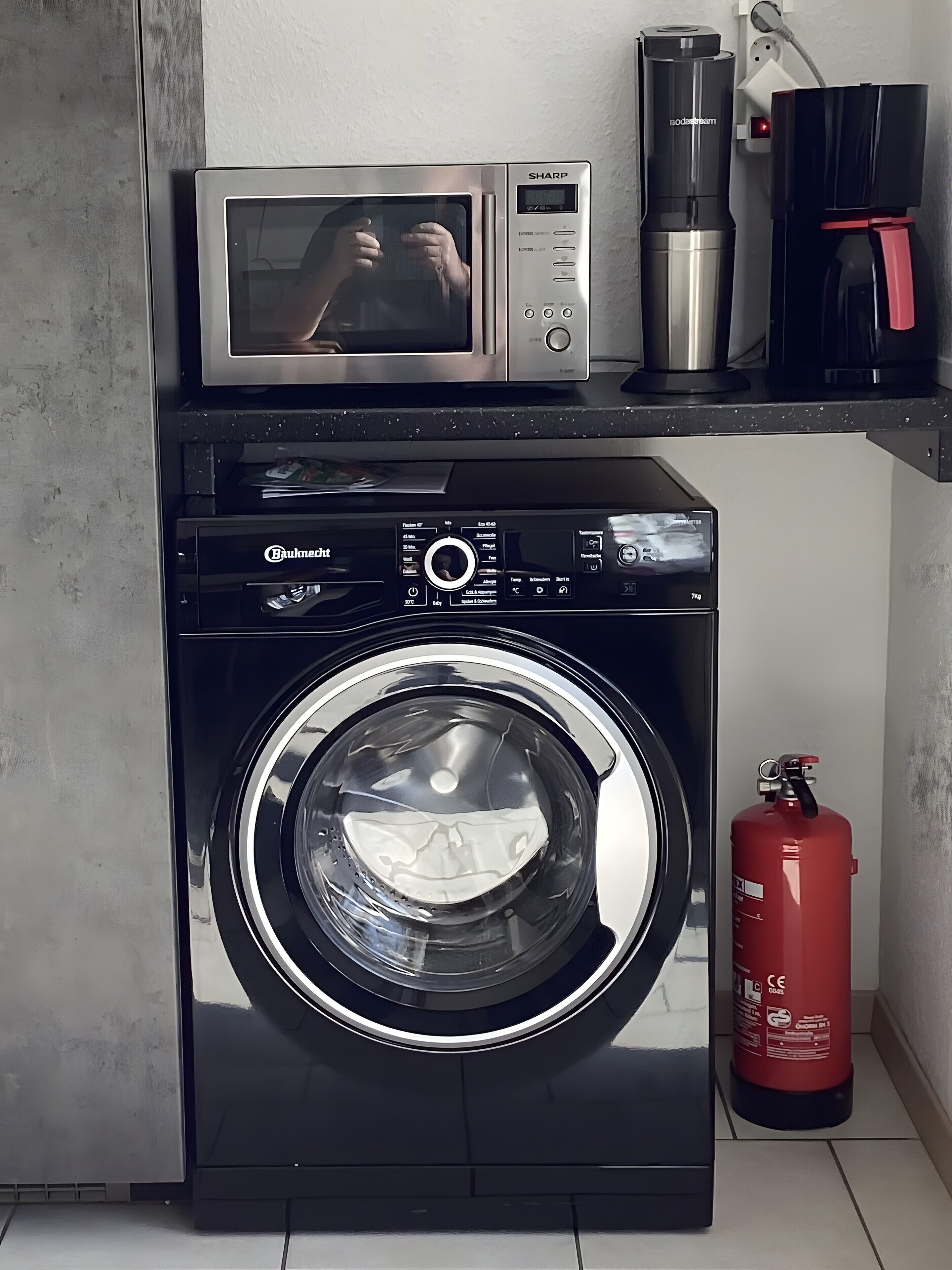 A compact laundry area with a washing machine, a microwave, and a coffee maker.