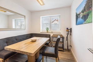 Une pièce moderne avec une table à manger en bois, des sièges rembourrés, un grand miroir, une fenêtre avec des stores et une lampe fixée au mur.