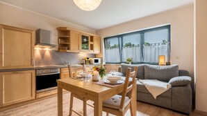 Una cocina moderna con armarios de madera, una mesa de comedor con sillas, un sofá gris y un ventanal con cortinas.