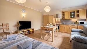 Un apartamento moderno con sala de estar, comedor y cocina. Hay un televisor, muebles de madera y un reloj en la pared.