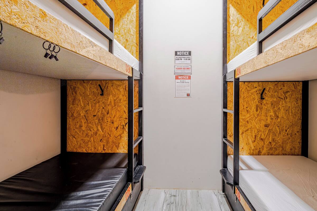 Quarto com beliche, quadro de avisos, paredes de madeira e escada de metal.