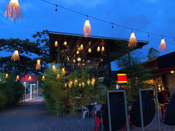 Un espacio al aire libre con luces colgantes, una zona de estar techada y un letrero de restaurante.