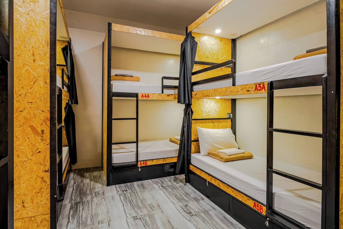 Quarto com beliche, paredes e chão de madeira, cortina preta e colchão branco.