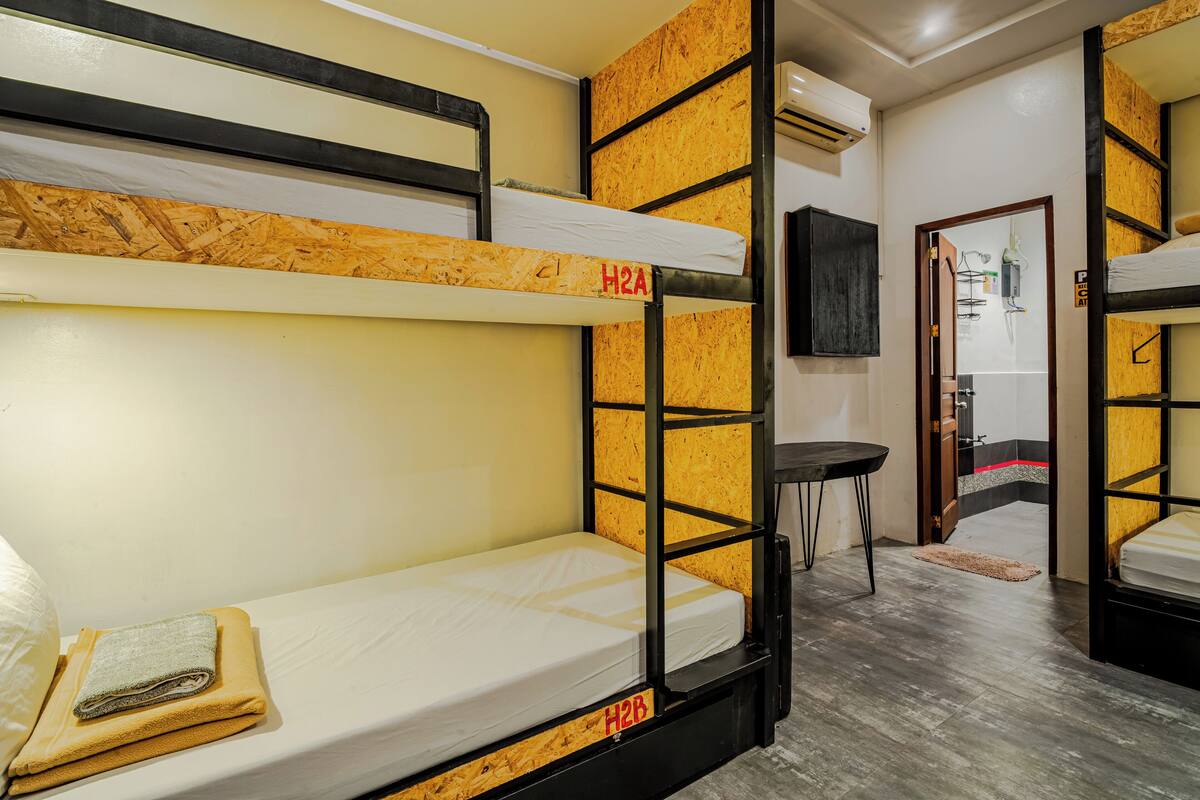 Quarto com beliche, cabeceira de madeira, uma mesinha e porta que dá para outro quarto.