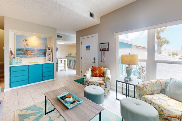 A living room with a view of the beach, a kitchen with blue cabinets, and a dining area with a table and chairs.