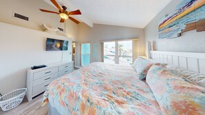 Un dormitorio con cama, ventilador de techo, televisor, cómoda y ventana con vistas al exterior.