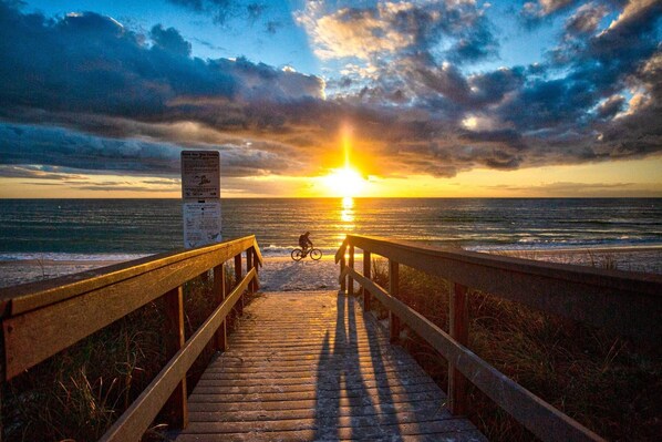 A wooden boardwalk leading to the ocean with a sunset in the background.
