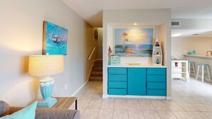 Una sala de estar con un sofá color turquesa, una lámpara y un cuadro de un paisaje marino.