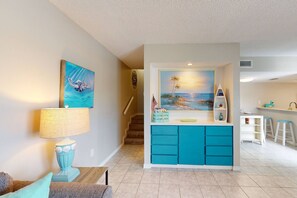 A living room with a teal sofa, a lamp, and a painting of a seascape.
