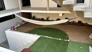 Un espacio exterior moderno con una hamaca, césped artificial y plantas en macetas.