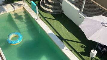 Une piscine avec un flotteur bleu gonflable, des marches menant à une terrasse et un parasol blanc.