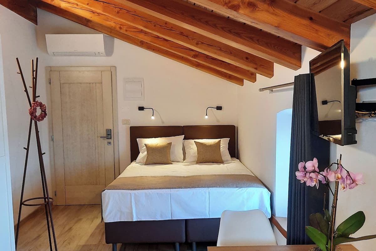 Een slaapkamer met een houten plafond, een bed met wit beddengoed, twee bedlampjes, een deur en een potorkidee.
