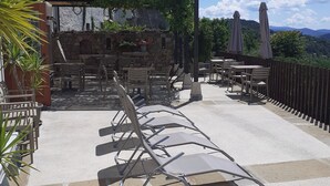 An outdoor patio with lounge chairs, tables, and umbrellas, surrounded by stone walls and greenery.