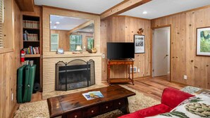 Ein gemütliches Wohnzimmer mit Holzwänden, einem Kamin, einem Fernseher und einem Bücherregal.