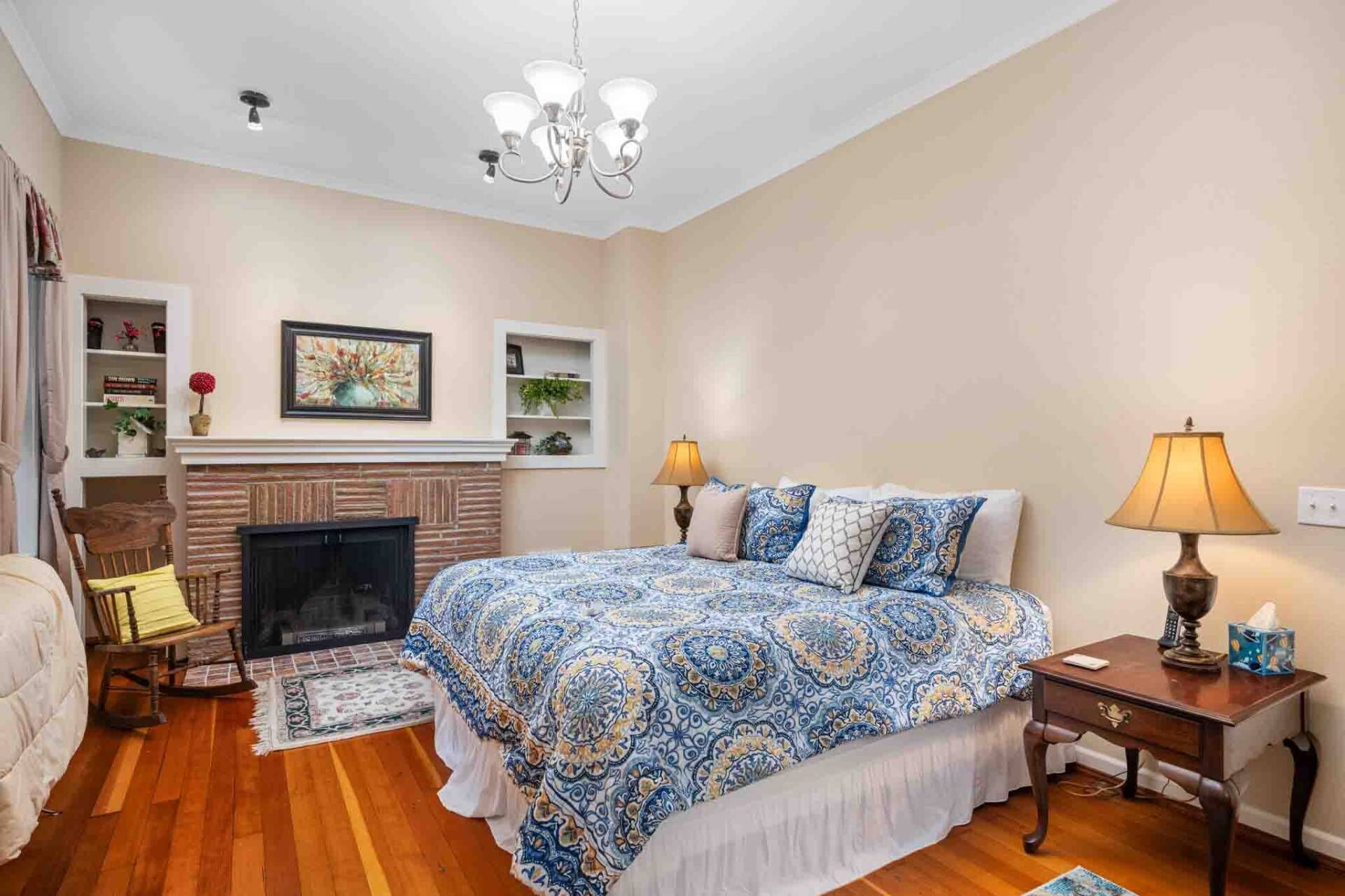 Une chambre à coucher avec un grand lit, une cheminée, un lustre et une table de chevet avec une lampe.