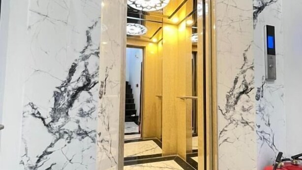 Een lift met een moderne inrichting, een zichtbare noodtelefoon en een rode brandblusser aan de rechterkant, geheel betegeld met marmer.