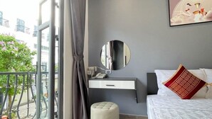 Een moderne slaapkamer met een groot bed, een nachtkastje, een spiegel en uitzicht op de stad vanuit een balkon.