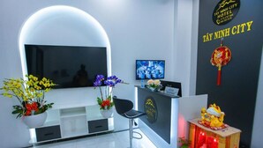 Een modern ingerichte hotelreceptie met een receptiebalie, een televisiescherm en een decoratief altaar met culturele symbolen.