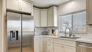 A modern kitchen with white cabinets, stainless steel appliances, and a window with blinds.