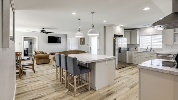 A modern kitchen with a central island, wooden flooring, pendant lighting, and a dining area with a sofa and chairs.