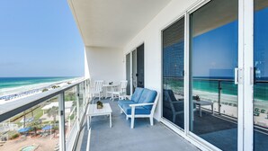 Een balkon met uitzicht op het strand, witte meubels en een zwembad.