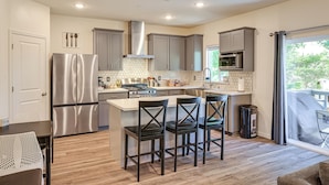 A modern kitchen with stainless steel appliances, a central island with bar stools, and a view through a large window. - Spacious Family Home in Stockton - Pets Welcome! (Stockton)