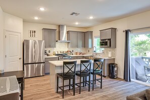 A modern kitchen with stainless steel appliances, a central island with bar stools, and a view through a large window. - Spacious Family Home in Stockton - Pets Welcome! (Stockton)