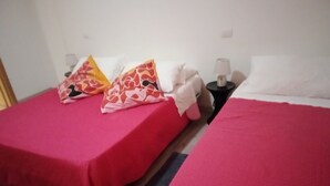 Dos camas individuales con ropa de cama roja, una mesita de noche con lámpara y un cojín estampado.