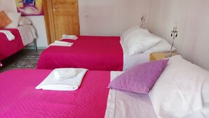 Habitación de hotel con dos camas, cada una con una colcha rosa y almohadas blancas. Hay toallas enrolladas sobre las camas.