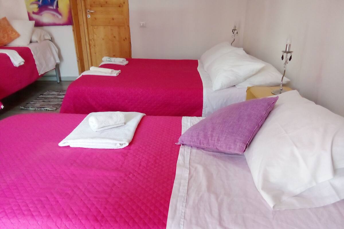 Habitación de hotel con dos camas, cada una con una colcha rosa y almohadas blancas. Hay toallas enrolladas sobre las camas.