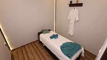 Cozy retreat with a single bed, green pillow, and teal towel, featuring a wall-mounted shelf and a hook for your belongings.