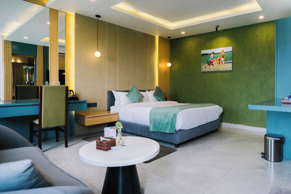 A modern hotel room with a bed, desk, chair, and a small table with a vase.