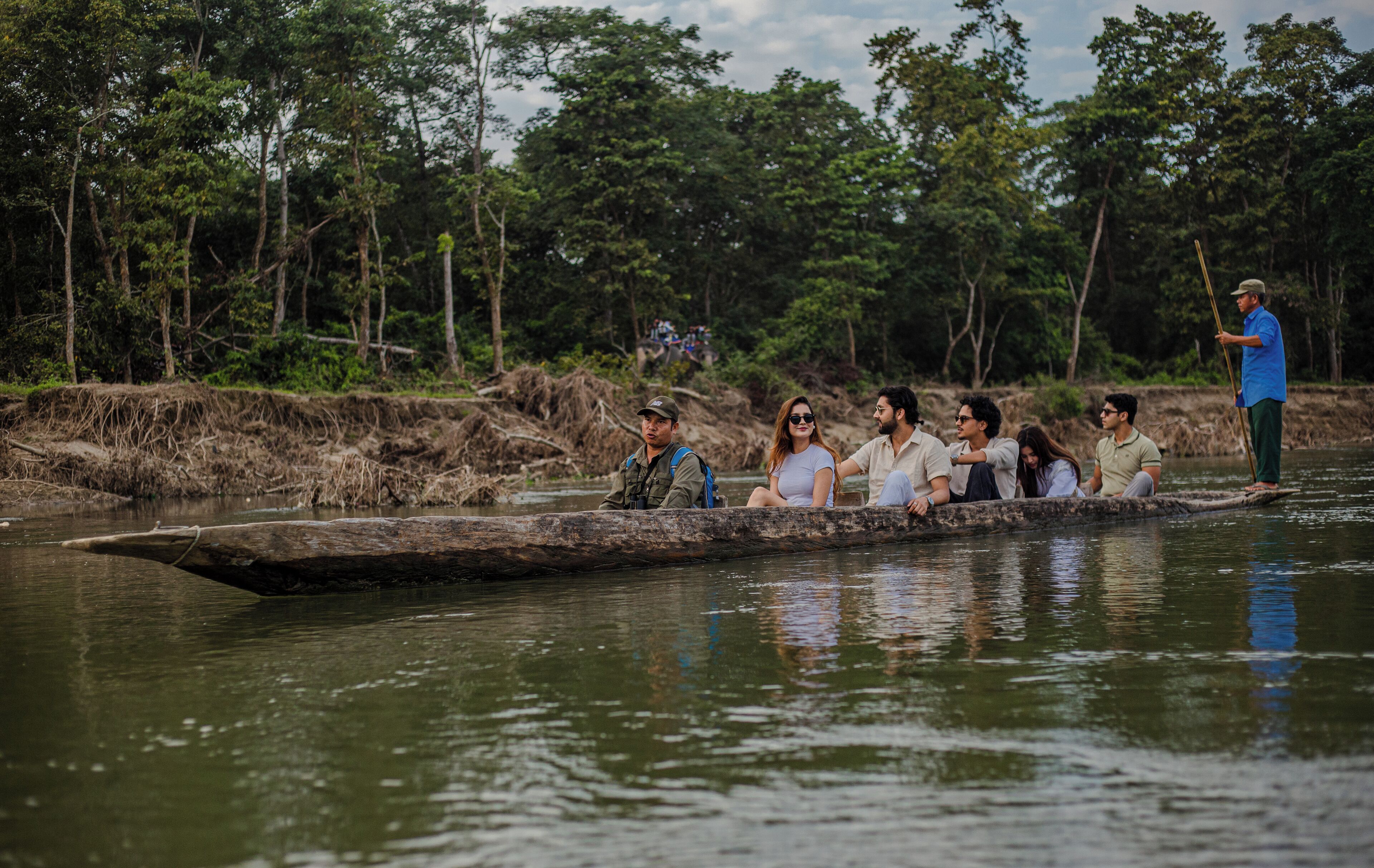 A group of people on a longboat in a river surrounded by dense forest.