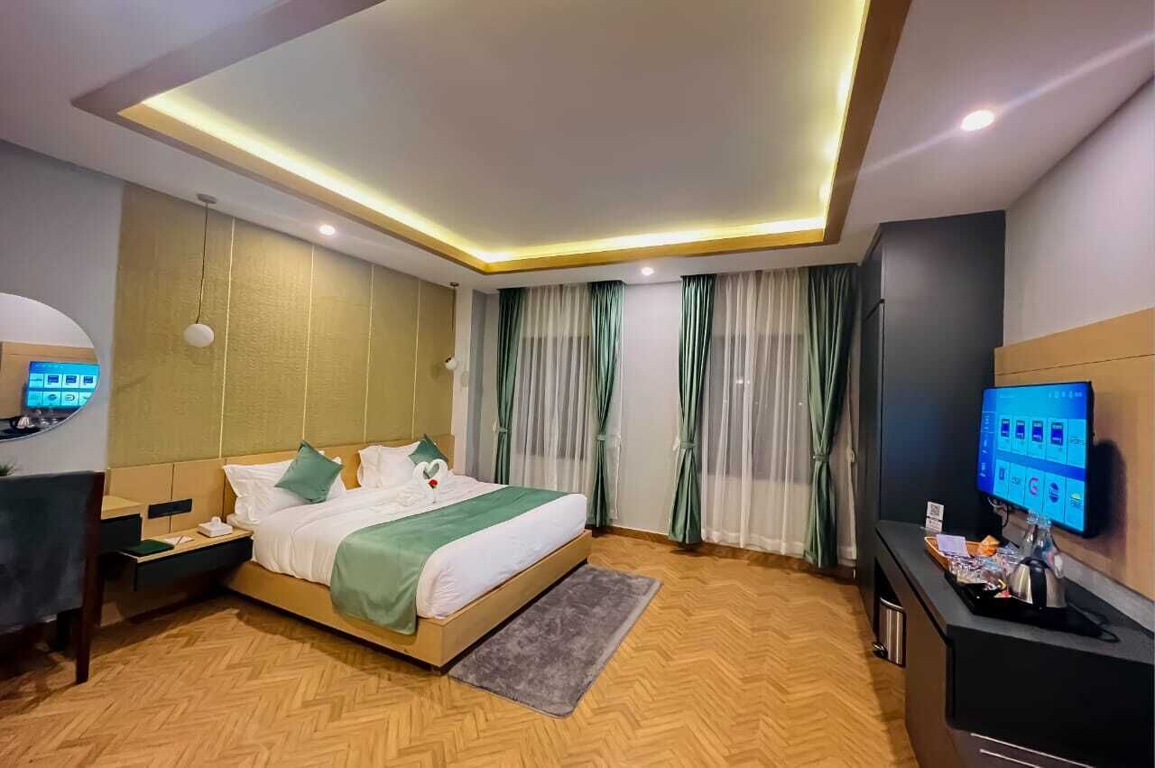 A modern hotel room with a bed, a desk, a television, and a desk lamp.