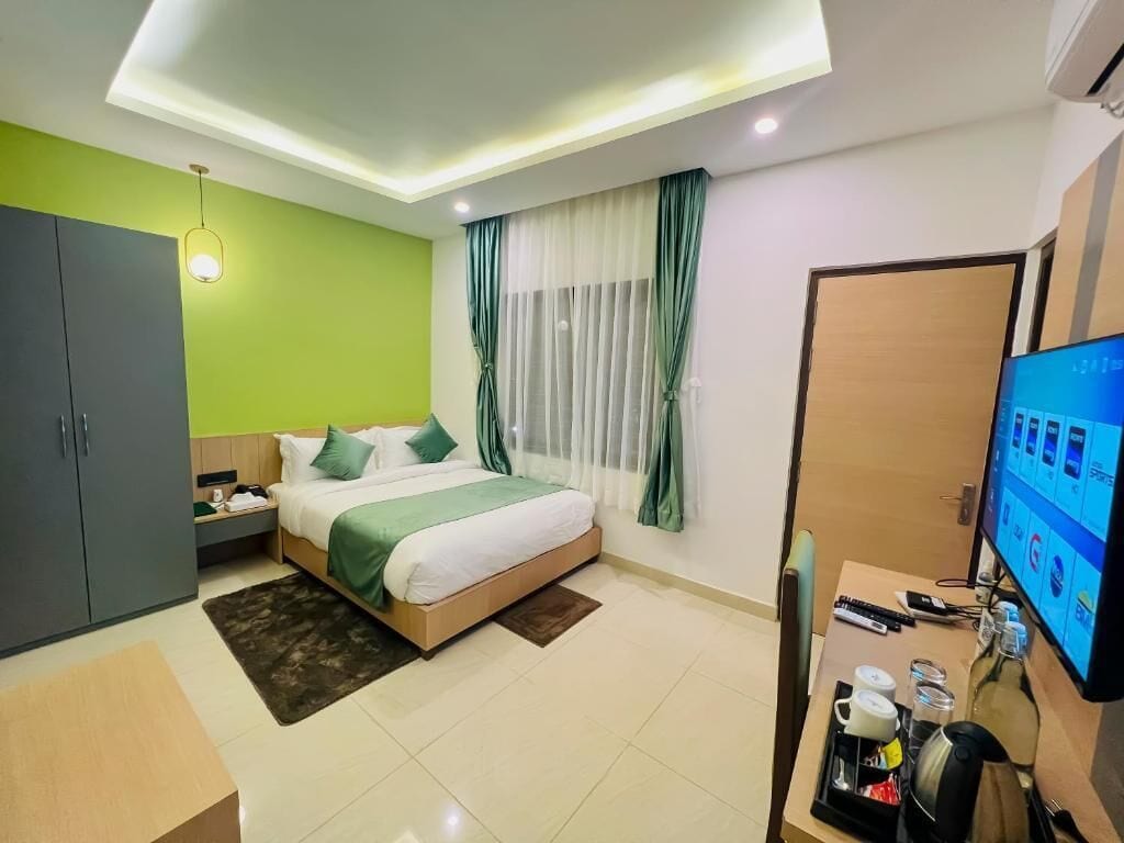 A hotel room with a bed, a desk with a computer, a wardrobe, and a TV.