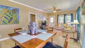 A dining area with a wooden table, chairs, and a decorative elephant sculpture. There is a television in the background, a sofa with cushions, and a ceiling fan. - Biloxi Home: Walk to Fishing & 2 Mi to Beach! (Biloxi)