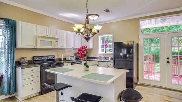 A kitchen with white cabinets, a black refrigerator, a stove, and a sink. There is a window with a view of greenery outside. - Biloxi Home: Walk to Fishing & 2 Mi to Beach! (Biloxi)