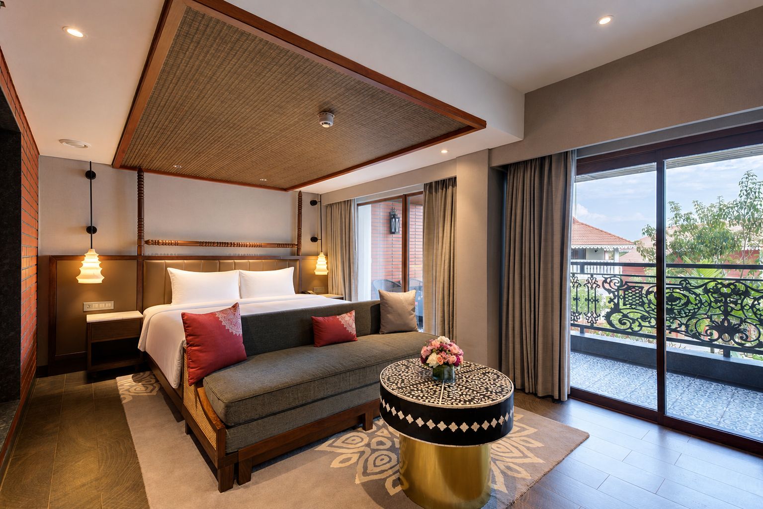 A hotel room with a bed, bedside tables, a sofa, a round coffee table, and a balcony with a view.