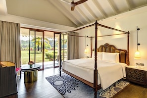 A four-poster bed with a nightstand, a small table with a vase, and a view of a garden through a sliding door. - Gateway Bekal (Hosdurg)