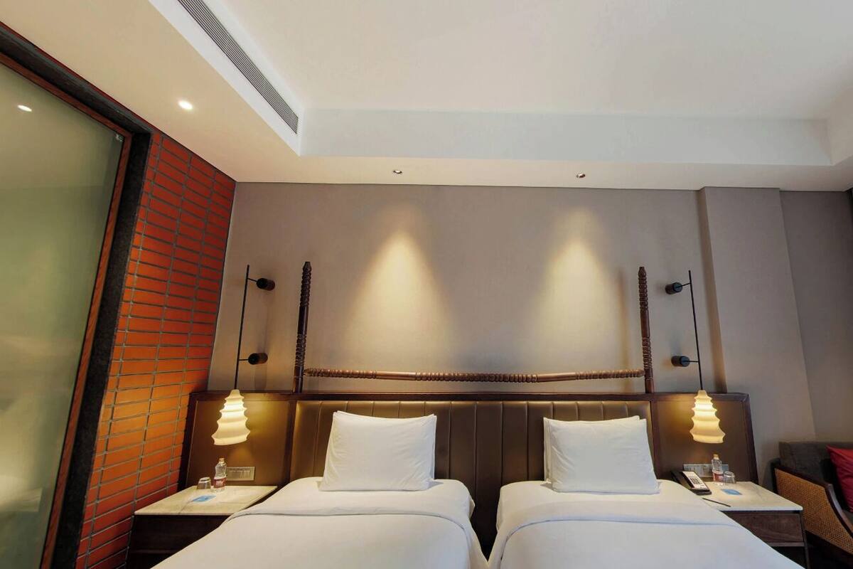 Ein Hotelzimmer mit zwei Betten, einer Ziegelwand, einem großen Fenster und einem Vorhang.