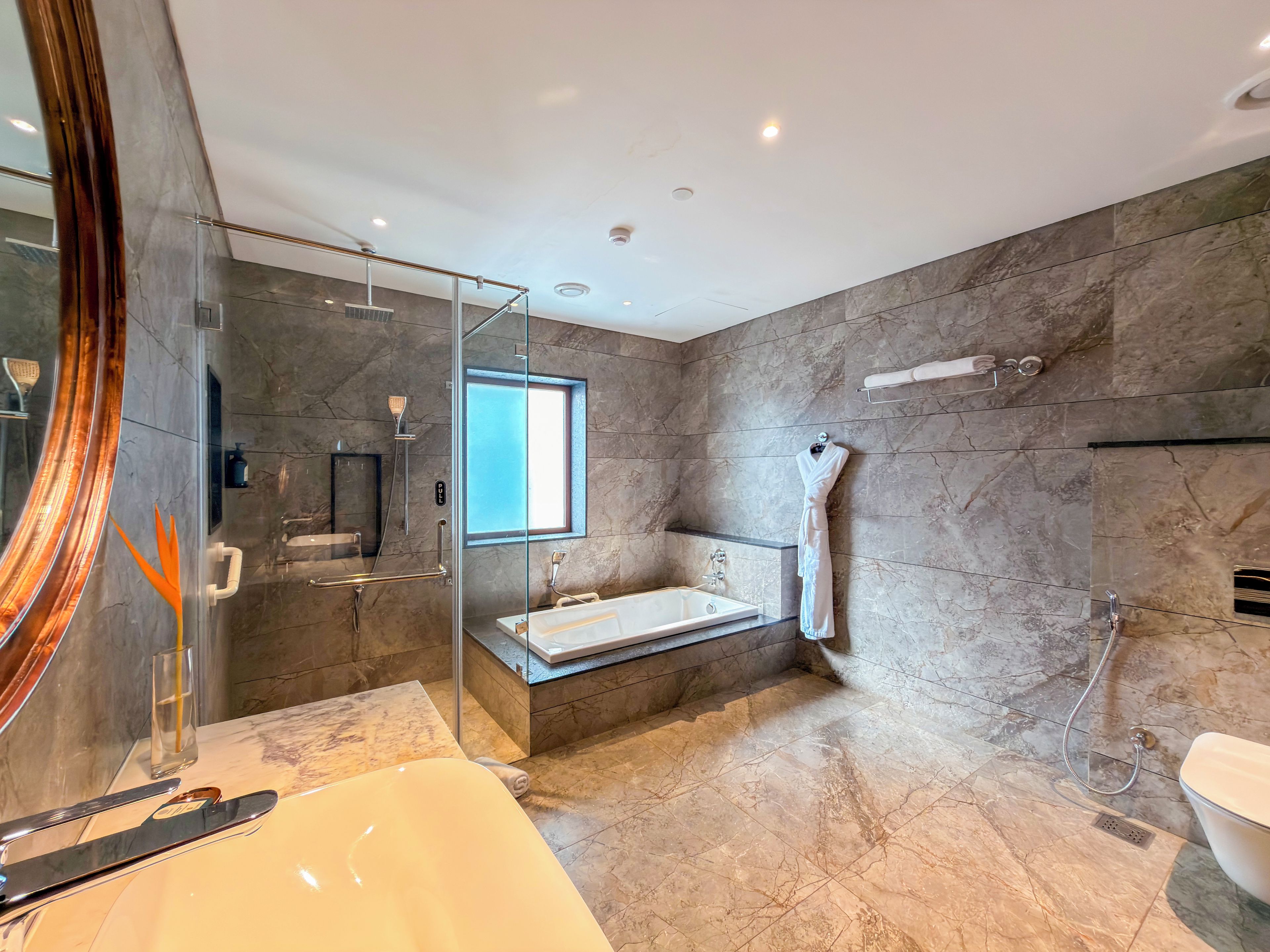 Un baño moderno con ducha envuelta en vidrio, bañera y un espejo grande.