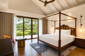 A four-poster bed with a wooden headboard, a dining table with a patterned table runner, and a view of a tropical garden through large sliding doors. - Gateway Bekal (Hosdurg)
