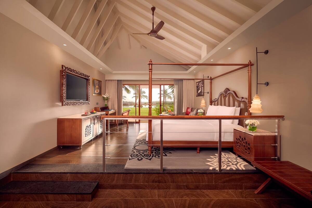 Ein Schlafzimmer mit Himmelbett, Deckenventilator, großem Fenster mit Blick auf Palmen und Holzboden.