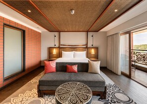A hotel room with a bed, bedside tables, a sofa, a patterned ottoman, and a balcony with a railing. - Gateway Bekal (Hosdurg)