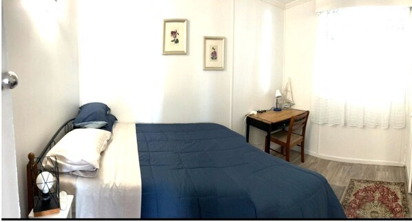 A bedroom with a bed, a desk, and two framed pictures on the wall.