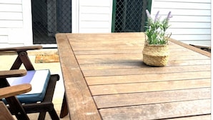 Um deck de madeira com uma mesa e cadeiras, uma cesta de palha com plantas e uma porta com moldura verde.
