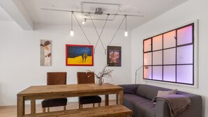 Un salon moderne avec une table à manger en bois, deux chaises, un canapé et des œuvres d’art accrochées aux murs.