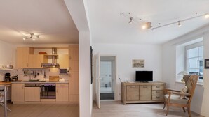 Une cuisine moderne dotée d’appareils électroménagers intégrés, un coin repas avec une table en bois et un téléviseur posé sur un meuble en bois.