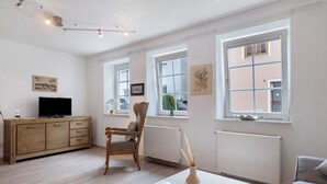 Un salon moderne avec un meuble en bois, un téléviseur, un fauteuil, une table et de grandes fenêtres.