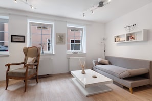 A modern living room with a wooden chair, a grey sofa, a white coffee table, and a white radiator.